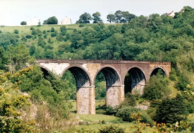 View from Monsal Head over the green valley of Monsal Dale, with the River Wye winding below and a railway viaduct crossing the dale