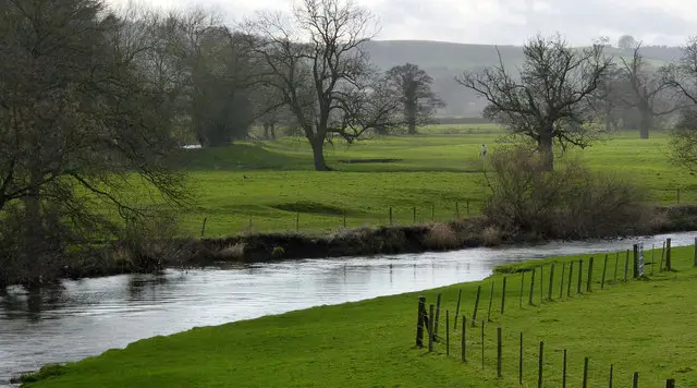 Ruined walls of Tutbury Castle rising above the River Dove and riverside paths in the Staffordshire village of Tutbury