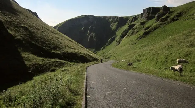 Walkers on a path above a steep-sided limestone pass with grassy hillsides rising on either side in the Derbyshire Hope Valley