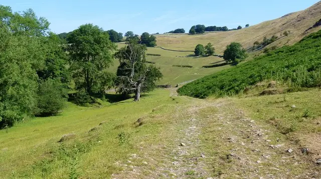 Walkers on a path near the River Manifold with the wooded hills around Ilam in the background